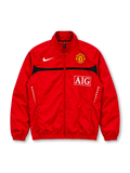 Front view of the Manchester United 2009/10 Nike red track jacket featuring a curved black chest stripe, white Nike Swoosh, Manchester United club crest, AIG sponsor logo, high collar, full-length front zipper, and two zippered pockets.