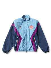 Paris Saint-Germain × Jordan Brand track jacket in ice blue with diagonal purple chevron panels, Jumpman logo at left chest, coral PSG crest badge at right chest, navy sleeves