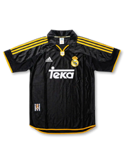 Front view of Real Madrid 1999-2000 away shirt in black with yellow trim, Teka sponsor, adidas logo, club crest, and polo collar.