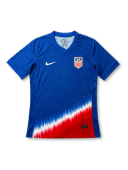 USA national team Nike 2024/25 away jersey in royal blue with tonal vertical pinstripe texture, dramatic diagonal red, white, and blue gradient fade at hem, white Swoosh at left chest, USA shield crest at right chest